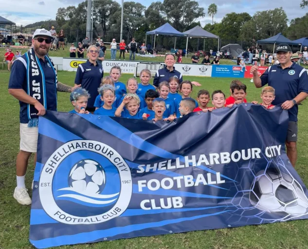 Shellharbour City Football Club players and coaches holding a club banner
